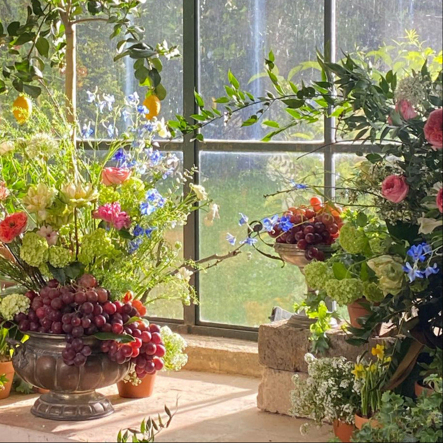 Atmosfera floreale con rose, ortensie, fiori azzurri e grappoli d’uva in ambiente luminoso