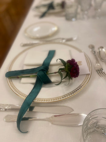 Dettaglio mise en place con fiore bordeaux e nastro verde su piatto decorato