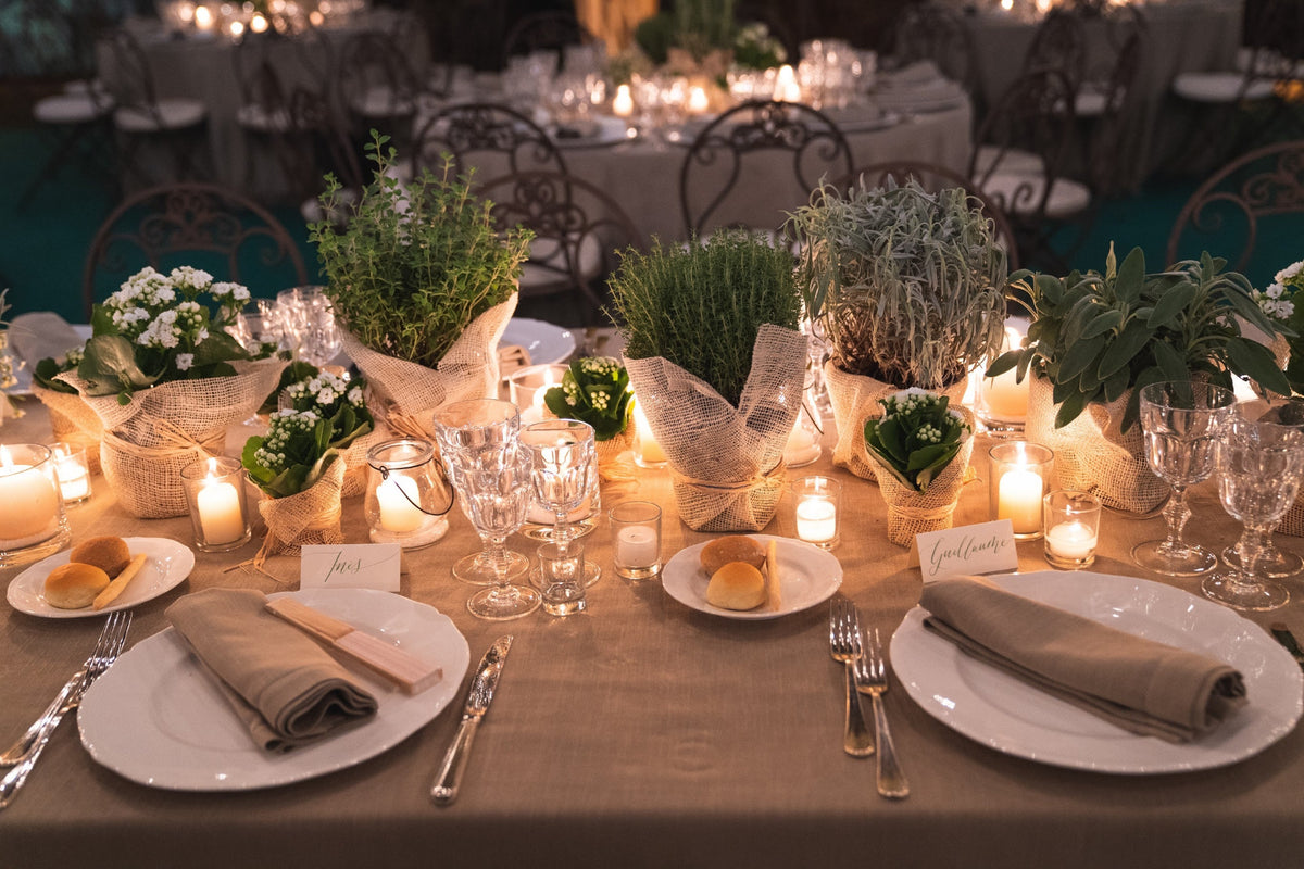 Tavolo da matrimonio con erbe aromatiche, piccole piante e candele in atmosfera serale